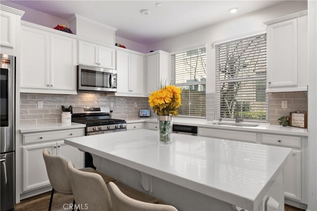 kitchen featuring appliances with stainless steel finishes, a kitchen breakfast bar, light countertops, white cabinetry, and a sink