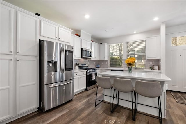 kitchen with dark wood-style floors, a breakfast bar, stainless steel appliances, light countertops, and white cabinetry