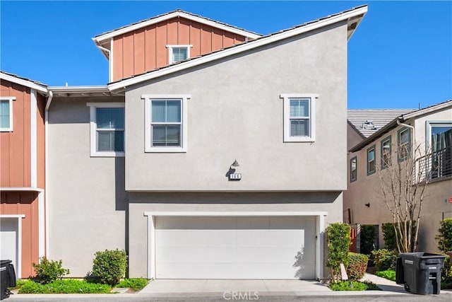 view of property featuring a garage, driveway, board and batten siding, and stucco siding