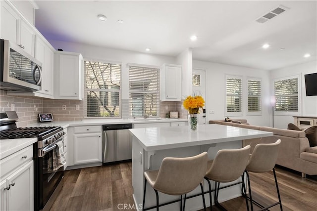 kitchen with open floor plan, stainless steel appliances, dark wood-type flooring, and visible vents