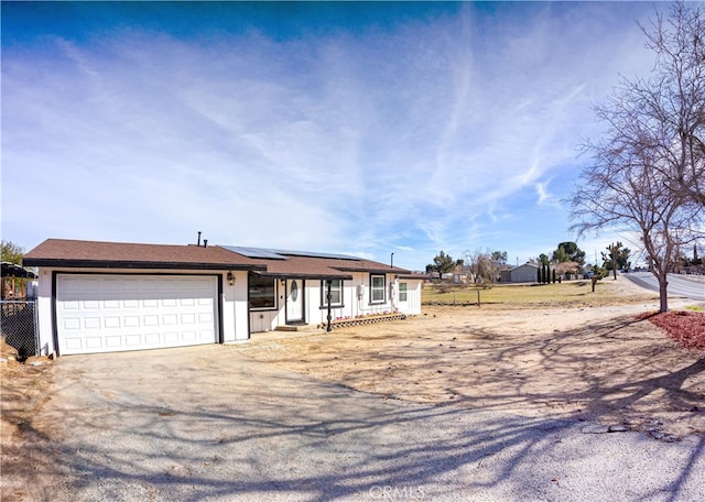 ranch-style house featuring a garage, driveway, fence, and roof mounted solar panels