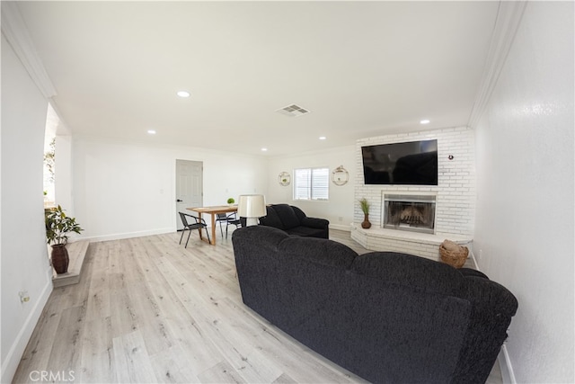 living room featuring crown molding, a fireplace, light wood finished floors, visible vents, and baseboards