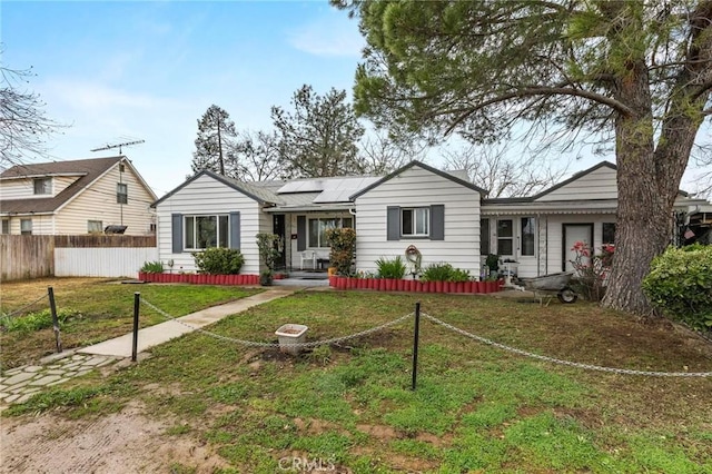 ranch-style house with roof mounted solar panels, fence, and a front lawn