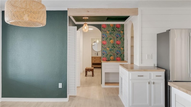 interior space with baseboards, arched walkways, ornamental molding, and light wood finished floors