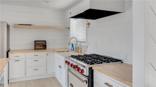 kitchen featuring butcher block countertops, stainless steel range with gas cooktop, wall chimney range hood, and open shelves