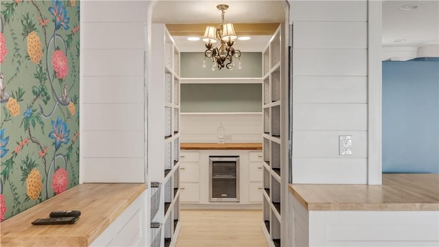 kitchen with white cabinetry, beverage cooler, a chandelier, and butcher block counters