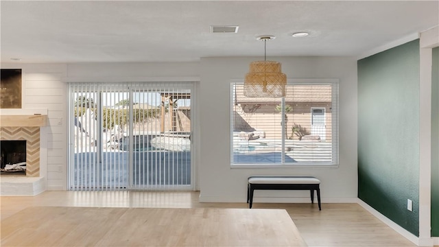 dining room featuring wood finished floors, a fireplace with raised hearth, visible vents, and baseboards