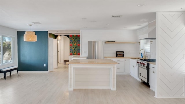 kitchen with light wood-style flooring, appliances with stainless steel finishes, arched walkways, white cabinets, and open shelves