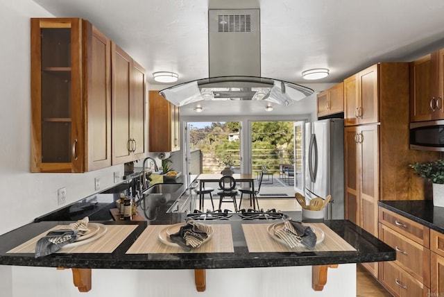 kitchen featuring a kitchen bar, island exhaust hood, appliances with stainless steel finishes, and a sink