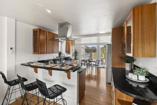 kitchen with a breakfast bar, stainless steel appliances, brown cabinetry, island range hood, and a peninsula