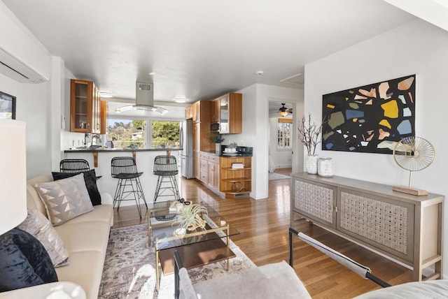 living room featuring ceiling fan, light wood-style flooring, and an AC wall unit