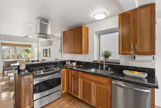 kitchen with brown cabinetry, wall chimney exhaust hood, appliances with stainless steel finishes, a peninsula, and a sink