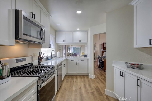 kitchen with light wood finished floors, light countertops, appliances with stainless steel finishes, white cabinets, and a sink