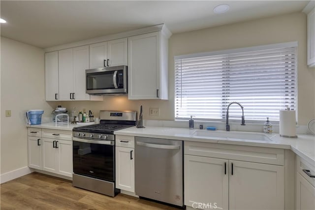 kitchen featuring a sink, white cabinetry, stainless steel appliances, light wood-style floors, and light countertops