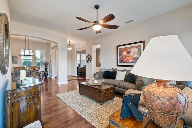 living room with dark wood-style floors, arched walkways, visible vents, and ceiling fan with notable chandelier