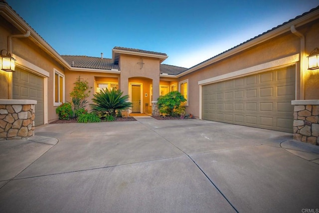 mediterranean / spanish house featuring a garage, a tile roof, stucco siding, and driveway