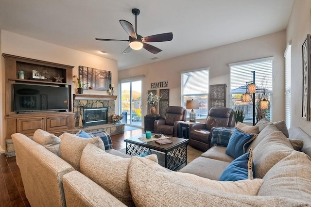 living area with wood finished floors, a ceiling fan, visible vents, and a stone fireplace