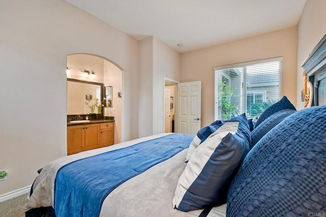 carpeted bedroom with arched walkways, a sink, ensuite bath, and baseboards