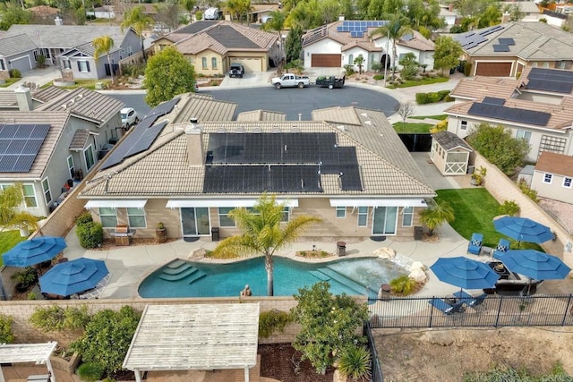 back of property with a fenced backyard, a fenced in pool, a residential view, roof mounted solar panels, and a tile roof