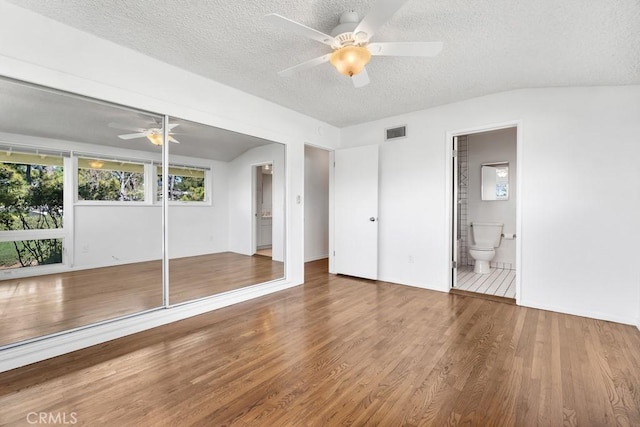 unfurnished bedroom with connected bathroom, a textured ceiling, visible vents, and wood finished floors