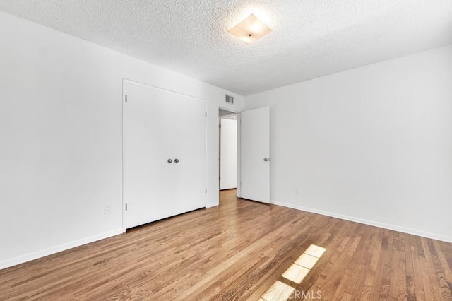 unfurnished room featuring visible vents, a textured ceiling, baseboards, and wood finished floors