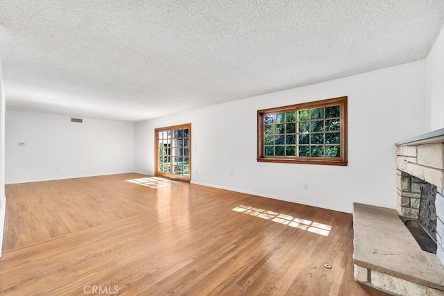 unfurnished living room with a textured ceiling, a fireplace, visible vents, and wood finished floors