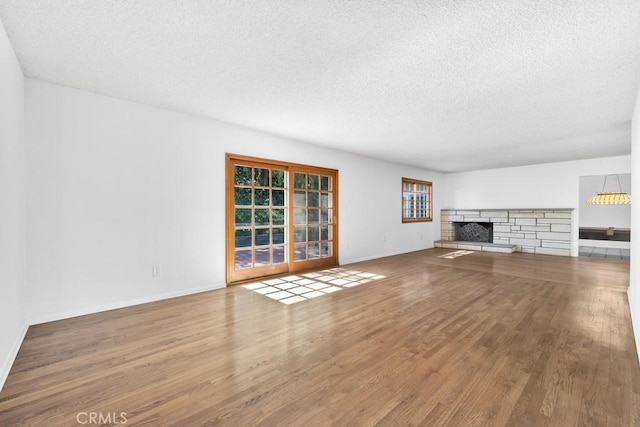 unfurnished living room with a textured ceiling, a fireplace, baseboards, and wood finished floors