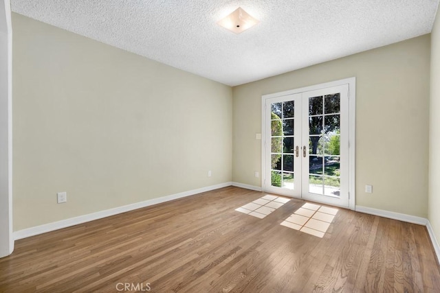 spare room with a textured ceiling, french doors, wood finished floors, and baseboards