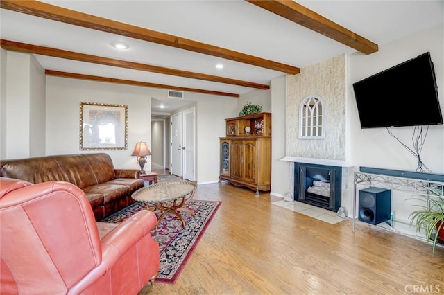 living area featuring baseboards, visible vents, wood finished floors, a fireplace, and beam ceiling