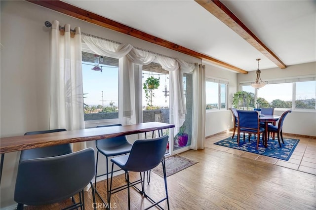 dining room with light wood finished floors, baseboards, and beamed ceiling