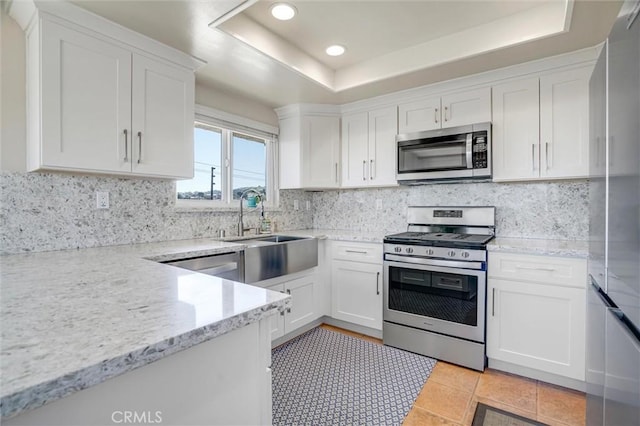 kitchen featuring white cabinets, appliances with stainless steel finishes, a raised ceiling, and decorative backsplash