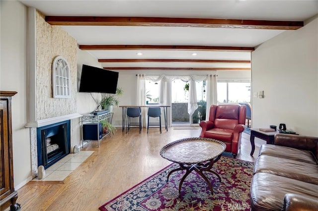 living area featuring light wood finished floors, a fireplace with flush hearth, baseboards, and beamed ceiling