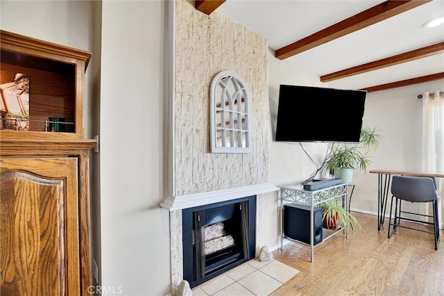 living room featuring a fireplace with flush hearth, baseboards, beamed ceiling, and wood finished floors