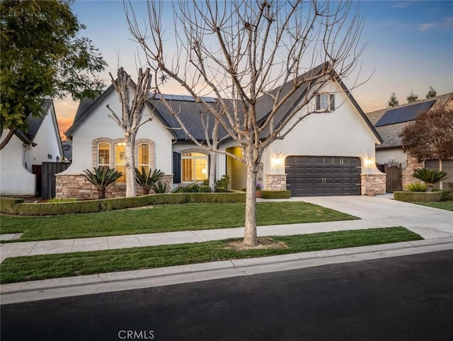 french country home with a yard, stucco siding, concrete driveway, an attached garage, and roof mounted solar panels