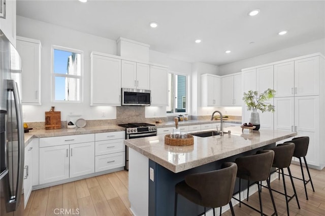 kitchen featuring light stone counters, appliances with stainless steel finishes, white cabinets, a sink, and a kitchen bar