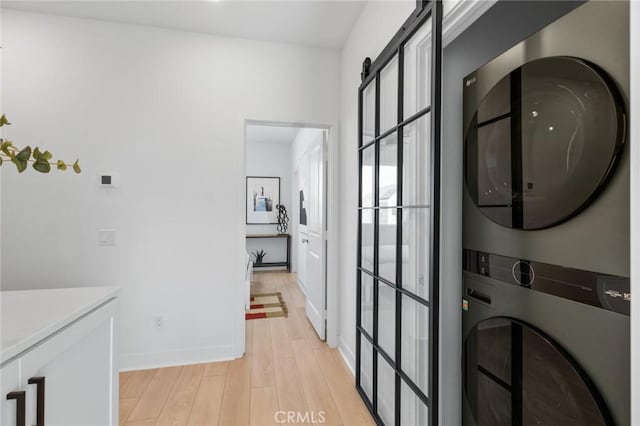 laundry area with light wood finished floors, stacked washer and dryer, cabinet space, a barn door, and baseboards