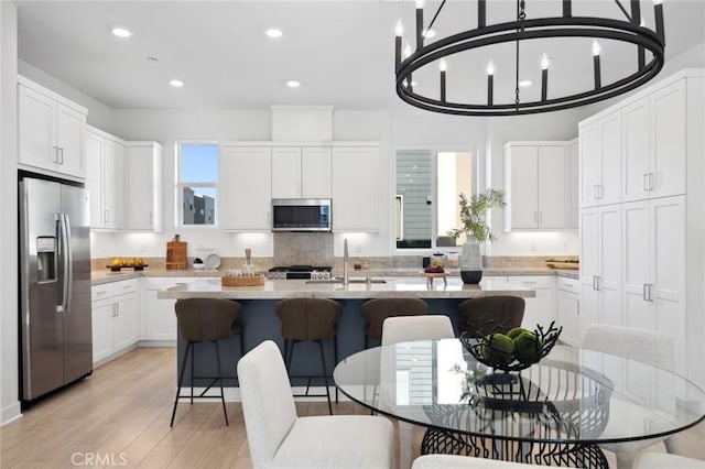 kitchen featuring a notable chandelier, appliances with stainless steel finishes, white cabinetry, a sink, and an island with sink