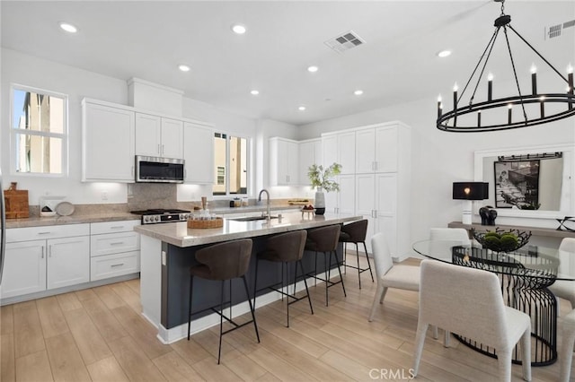 kitchen featuring stainless steel microwave, a sink, visible vents, and an island with sink