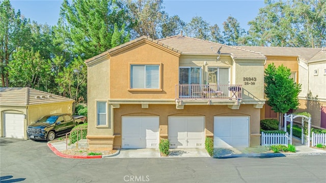 view of front facade featuring a garage, a balcony, a tile roof, fence, and stucco siding