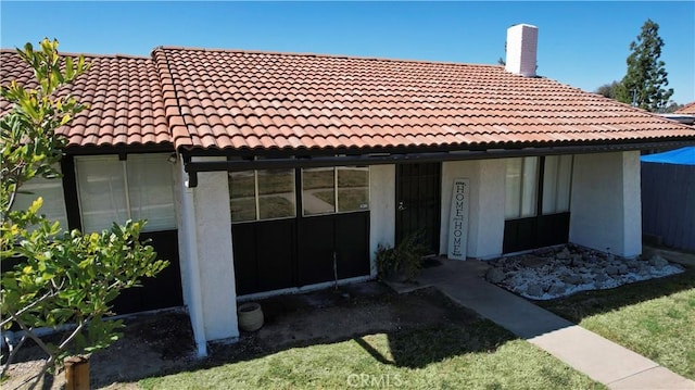 rear view of property featuring a tile roof, a chimney, and stucco siding