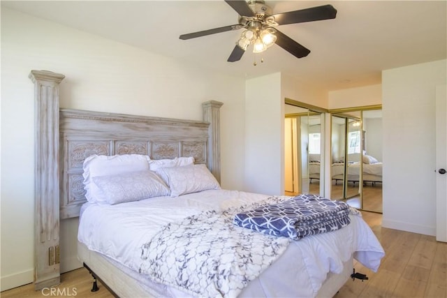 bedroom featuring a ceiling fan, baseboards, multiple closets, and wood finished floors