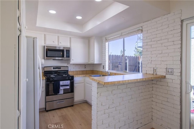 kitchen with a raised ceiling, stainless steel appliances, light countertops, light wood-type flooring, and white cabinetry