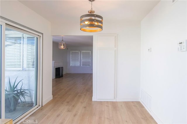 hall with light wood-type flooring, a notable chandelier, and baseboards