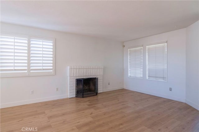 unfurnished living room with a brick fireplace, light wood-style flooring, and baseboards