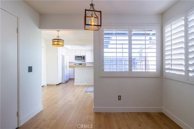 unfurnished dining area featuring baseboards and light wood-style floors