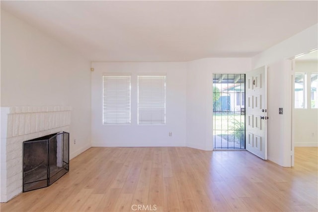 unfurnished living room with baseboards, a healthy amount of sunlight, a fireplace, and light wood finished floors