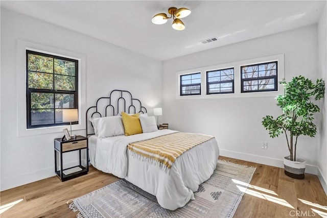 bedroom with wood finished floors, visible vents, and baseboards