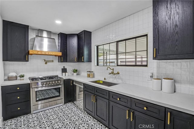 kitchen featuring light tile patterned floors, stainless steel appliances, tasteful backsplash, a sink, and wall chimney range hood