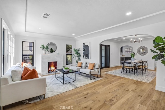 living room featuring arched walkways, a fireplace, visible vents, wood finished floors, and a chandelier