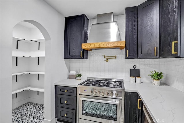 kitchen featuring light stone counters, stainless steel stove, wall chimney range hood, backsplash, and open shelves